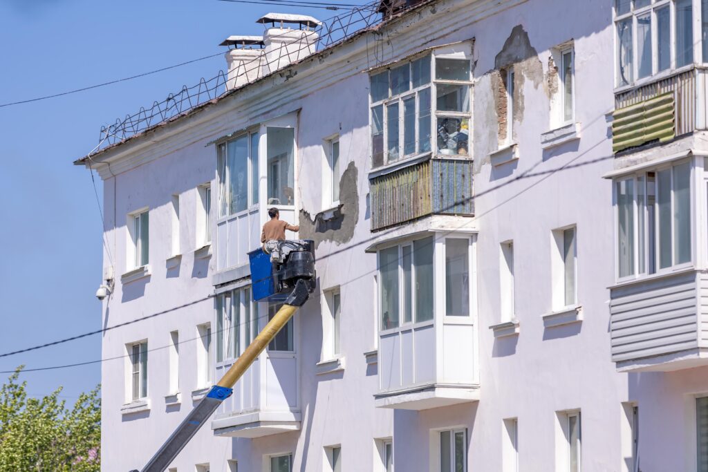 Worker renovating building facade using cherry picker on a sunny day.
