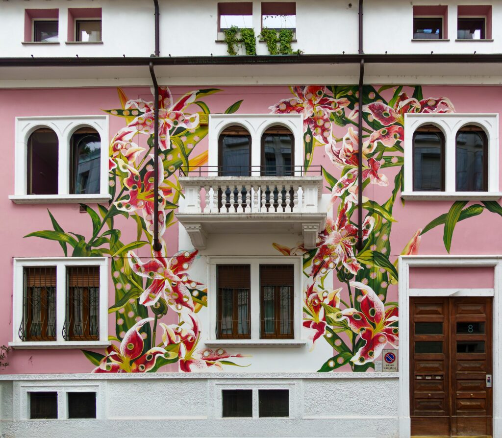 A colorful floral mural decorates the facade of a pink building with arched windows and a balcony.